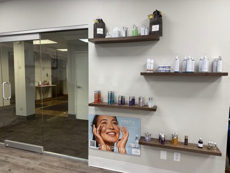 Wall shelves display skincare products above a Skinprint poster in a modern, clean office with glass doors.