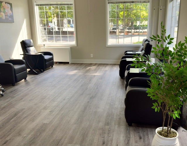 Bright waiting room with black chairs, large windows, wood flooring, and a potted plant in the foreground.